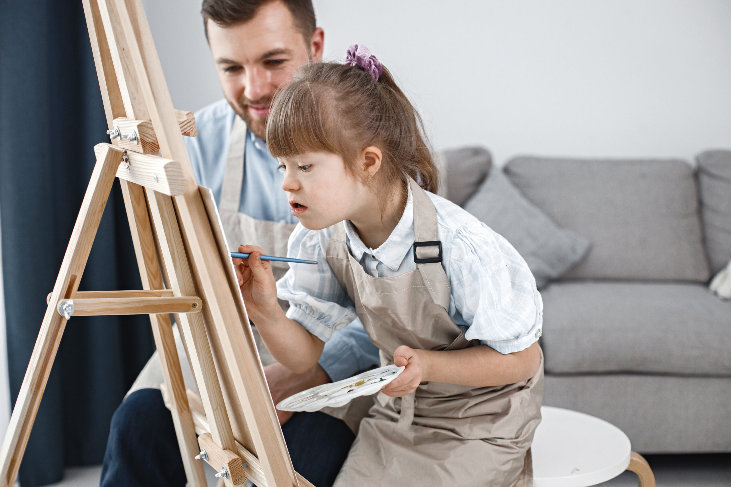 girl_with_down_syndrome_her_father_painting_easel_with_brushes-scaled